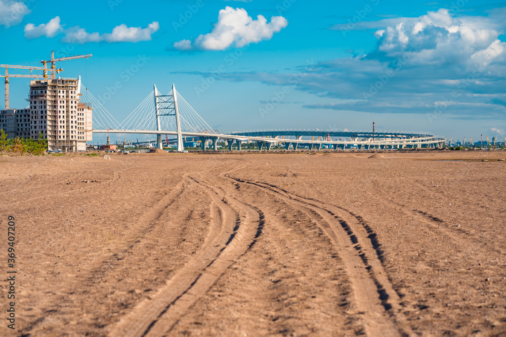 Tire tracks in the sand leading to the bridge and construction site in Petersburg