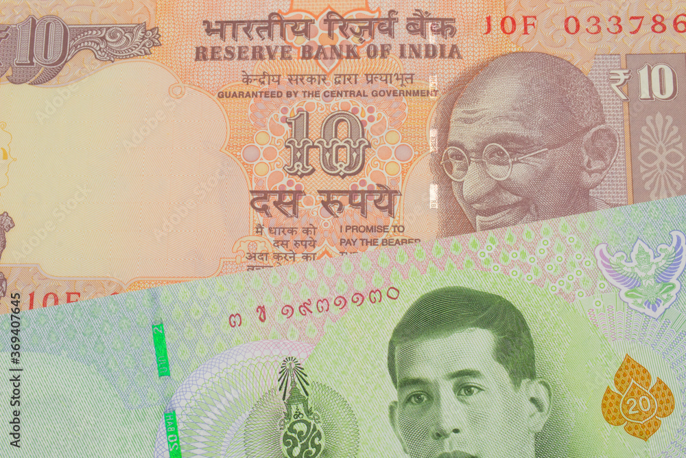 Fototapeta premium A macro image of a orange ten rupee bill from India paired up with a green twenty baht bank note from Thailand. Shot close up in macro.