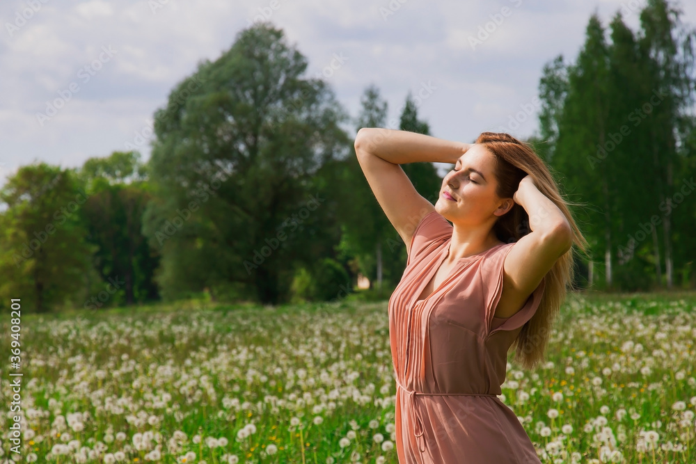 Young happy woman with her arms wide spread enjoys in the summer flower meadow white dandelions Young happy woman with her arms wide spread enjoys in the summer flower meadow white dandelions