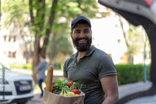 Young man with beard carrying  fresh groceries that he bought in super market from his trunk. 