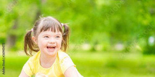 Portrait of a joyful little girl with syndrome down in a summer park. Empty space for text