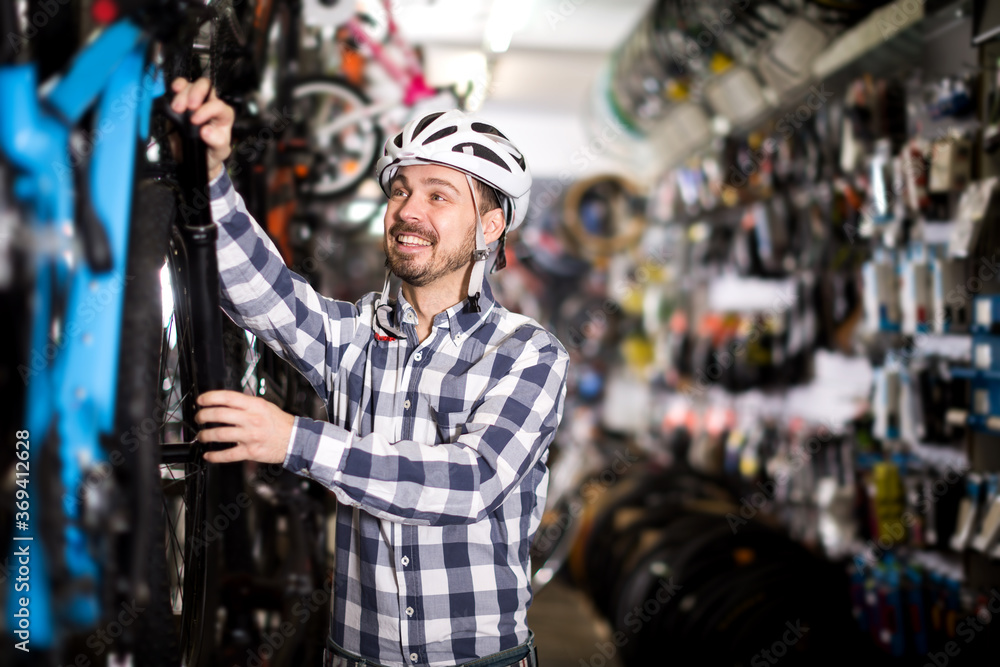 Happy young man in helmet chooses convenient bike to ride in sports store