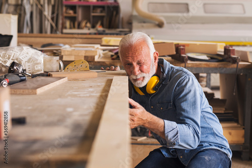Elderly woodworker checking evenness of a wooden plank