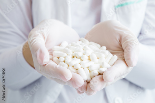 Doctor hands in rubber protective gloves holding white pills. Medical and pharmacy concept. Front view. Closeup.