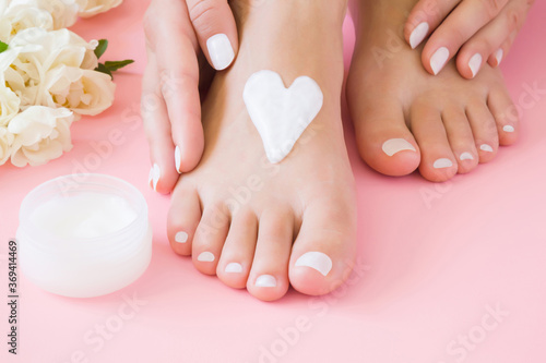 Young woman hands touching perfect groomed feet. Care about clean, soft, smooth skin. Heart shape created from natural herbal cream. Love body. Beautiful roses on pink background. Fresh flowers.