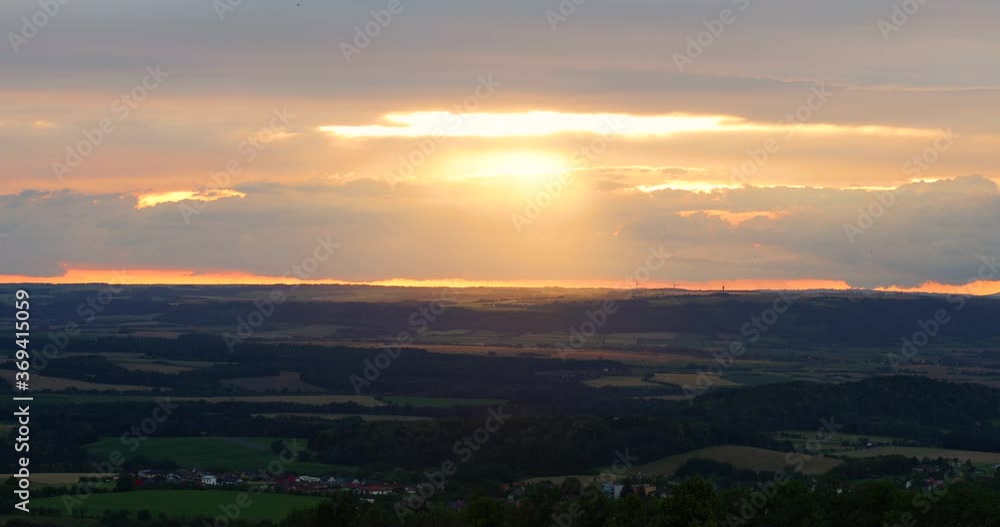 The sun shining through the clouds during sunset with the reflection of the rays into the landscape lying under clouds of different colors moving above the horizon. The sun shining through the clouds during sunset with the reflection of the rays into the landscape lying under clouds of different colors moving above the horizon.