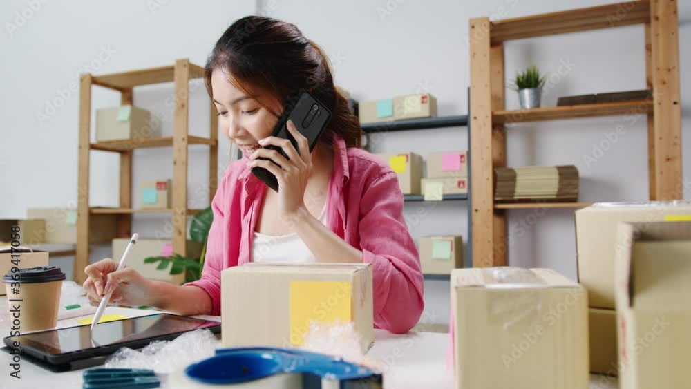 Young Asia businesswoman using mobile phone call receiving purchase order and check product on stock, work at home office. Small business owner, online market delivery, lifestyle freelance concept. Young Asia businesswoman using mobile phone call receiving purchase order and check product on stock, work at home office. Small business owner, online market delivery, lifestyle freelance concept.