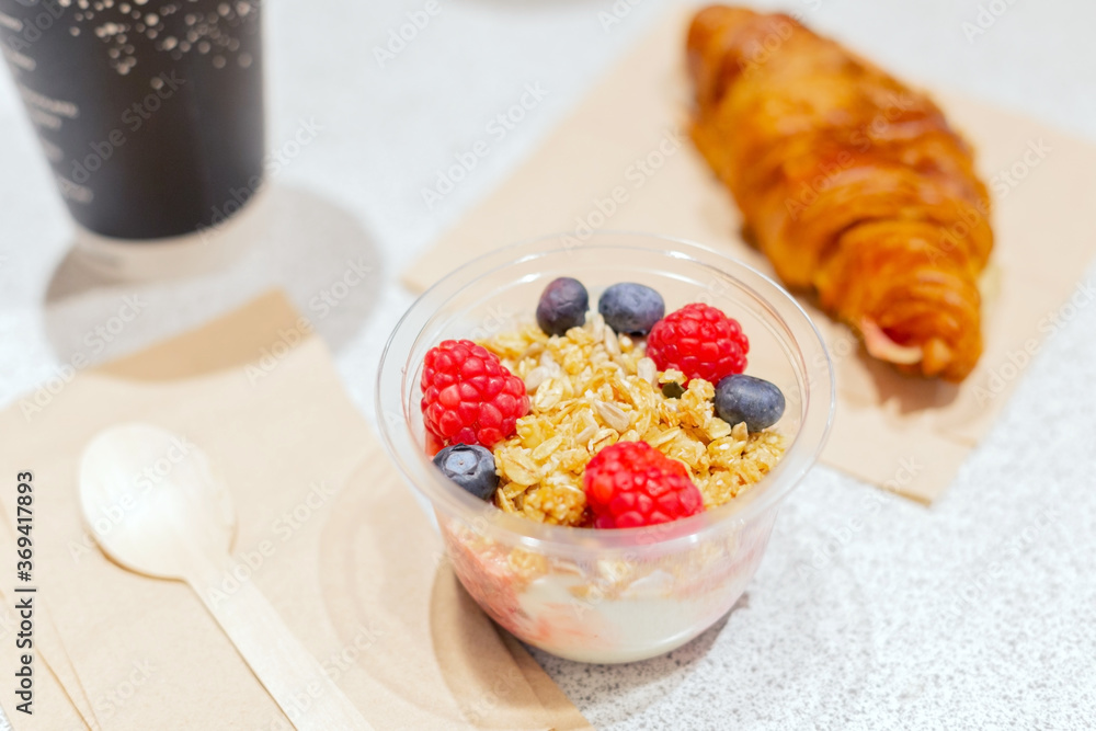 Jar of yogurt, jam, muesli, blueberries, raspberries a croissant, a Cup of coffee with you. Next to it is a spoon made of natural wood. Healthy ready-made Breakfast at the airport Jar of yogurt, jam, muesli, blueberries, raspberries a croissant, a Cup of coffee with you. Next to it is a spoon made of natural wood. Healthy ready-made Breakfast at the airport
