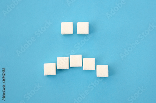 White sugar cubes laid out in the form of a sad smile on a blue background close-up. Concept of health, dentistry