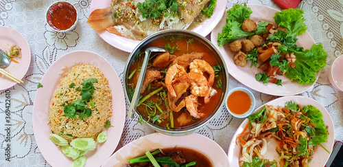 Flat lay of Thai food with fried rice, spicy salad, steamed fish and Sour soup with shrimp and mixed vegetables on the dining table. Top view of Asian food with spicy and sweet sauce.