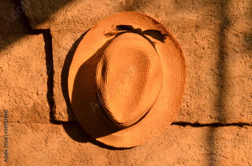 Cappello di paglia appeso ad un muro con la luce arancione del sole che tramonta.