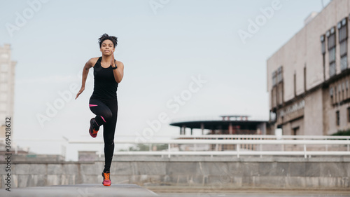 Sportswoman on street. Happy african american girl in sportswear with fitness tracker fast running © Prostock-studio