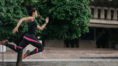 Healthy lifestyle and energy in body. Athlete african american girl in sportswear froze in air in jump, running at city