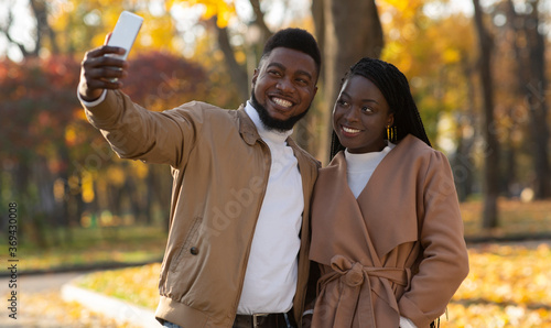 Afro couple in love taking selfie on date in autumn park