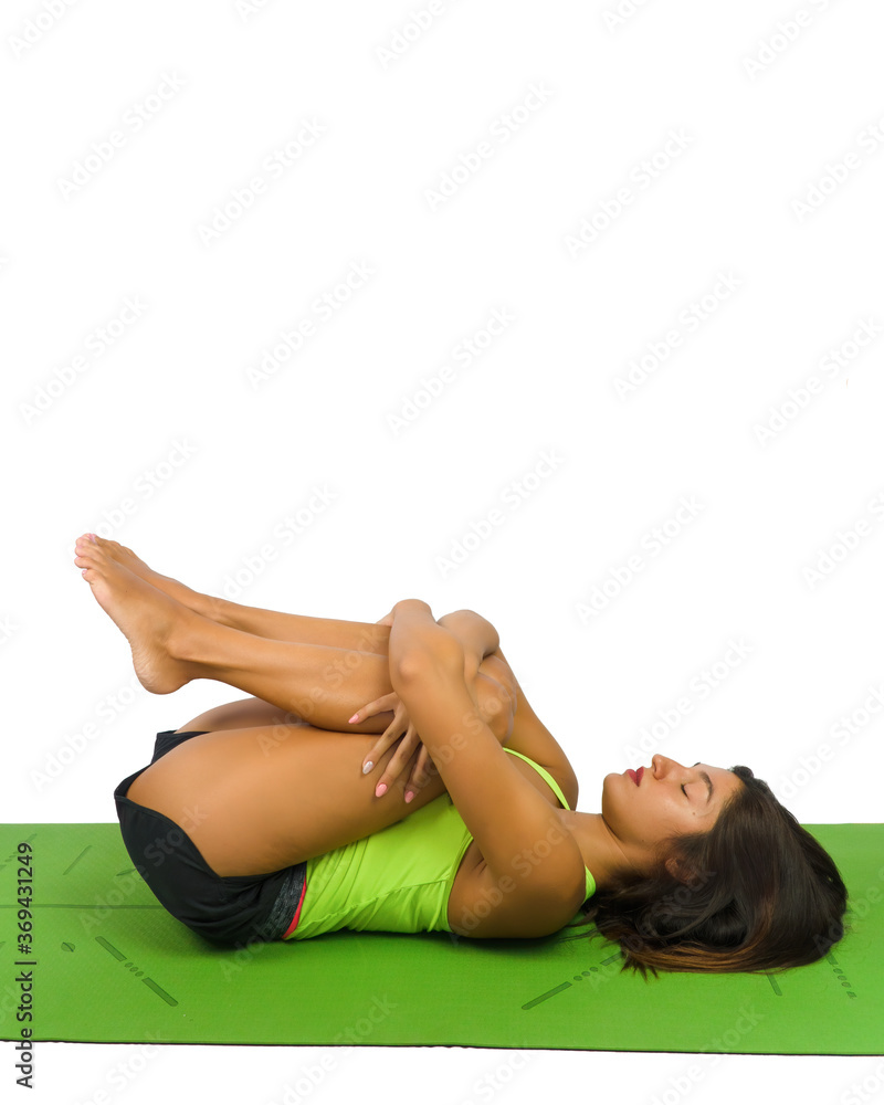 Naklejka premium A beautiful girl in shirt and shorts practices pilates at home on a green mat with legs gathered in her arms on her chest. Photos on a white background.