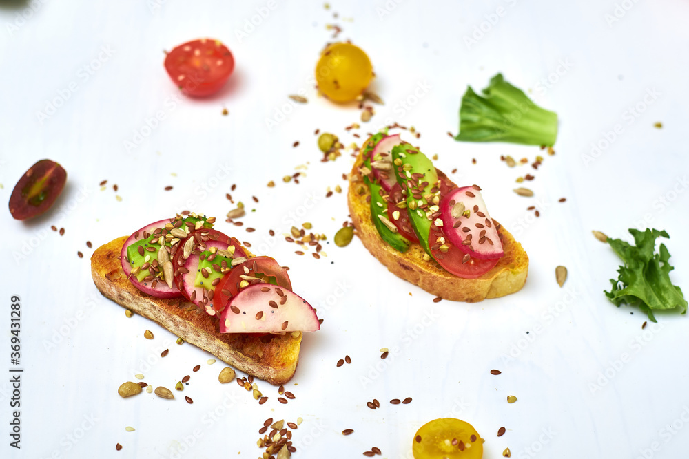 Toasts with vegetables, avocado, tomatoes, a set of seeds on a white background. Healthy food, diet concept. Toasts with vegetables, avocado, tomatoes, a set of seeds on a white background. Healthy food, diet concept.