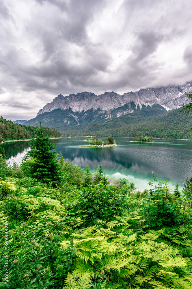 Small islands with pine-trees in the middle of Eibsee lake with Zugspitze mountain. Beautiful landscape scenery with paradise beach and clear blue water in German Alps, Bavaria, Germany, Europe. Small islands with pine-trees in the middle of Eibsee lake with Zugspitze mountain. Beautiful landscape scenery with paradise beach and clear blue water in German Alps, Bavaria, Germany, Europe.