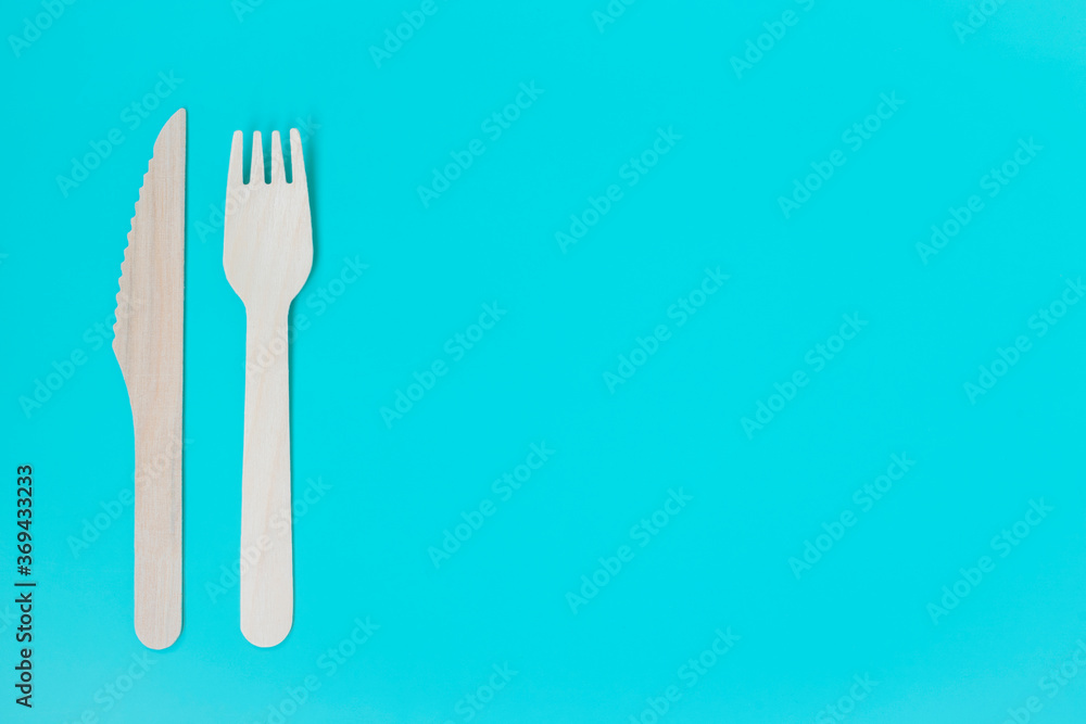 Craft. Craft disposable tableware. A wooden fork and knife lie on a turquoise background. Craft. Craft disposable tableware. A wooden fork and knife lie on a turquoise background.