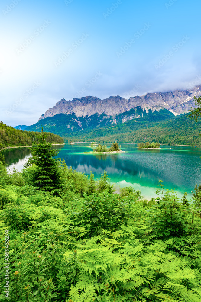 Small islands with pine-trees in the middle of Eibsee lake with Zugspitze mountain. Beautiful landscape scenery with paradise beach and clear blue water in German Alps, Bavaria, Germany, Europe. - obrazy, fototapety, plakaty 