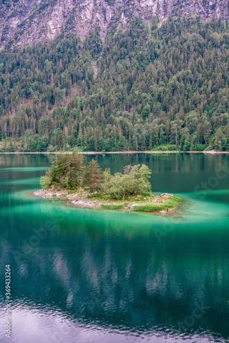 Small islands with pine-trees in the middle of Eibsee lake with Zugspitze mountain. Beautiful landscape scenery with paradise beach and clear blue water in German Alps, Bavaria, Germany, Europe.