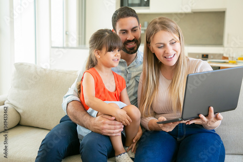 Happy family with kid using laptop for video call, talking to grandparents, looking at display while sitting on couch at home. Communication concept