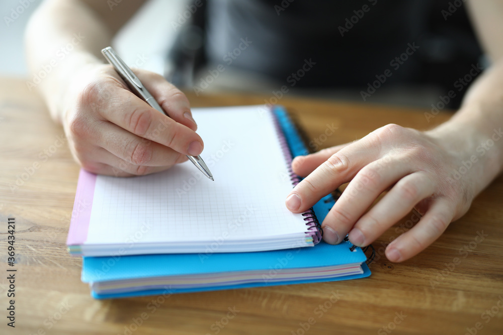 Male hands make notes in a notebook close up. Student guy holds a pen over a diary Male hands make notes in a notebook close up. Student guy holds a pen over a diary
