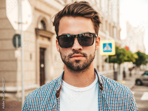 Portrait of handsome confident stylish hipster lambersexual model.Man dressed in shirt. Fashion male posing on the street background in sunglasses