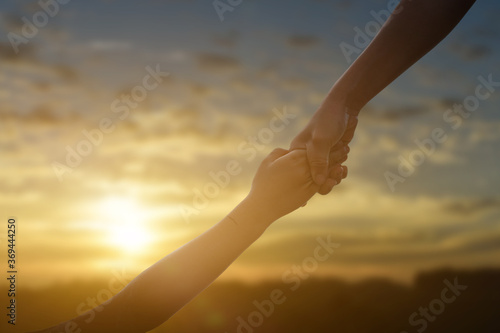 Silhouette of giving a help hand, hope and support each other over sunset background. Concept of helping hands and develop a friendship.