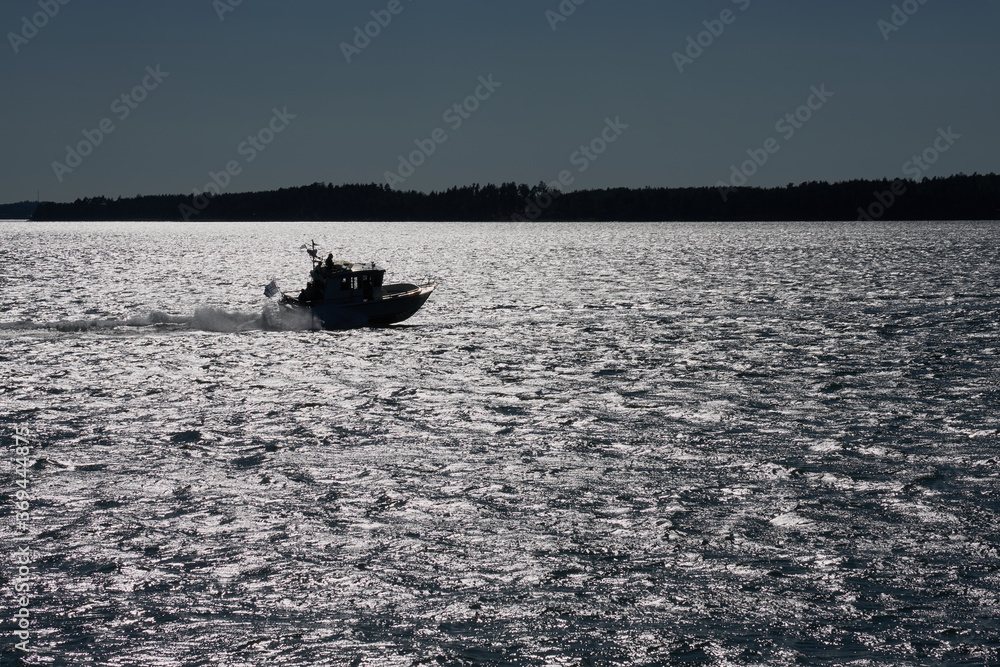 A silhouette of a boat going fast in sunlight glittering on water.
