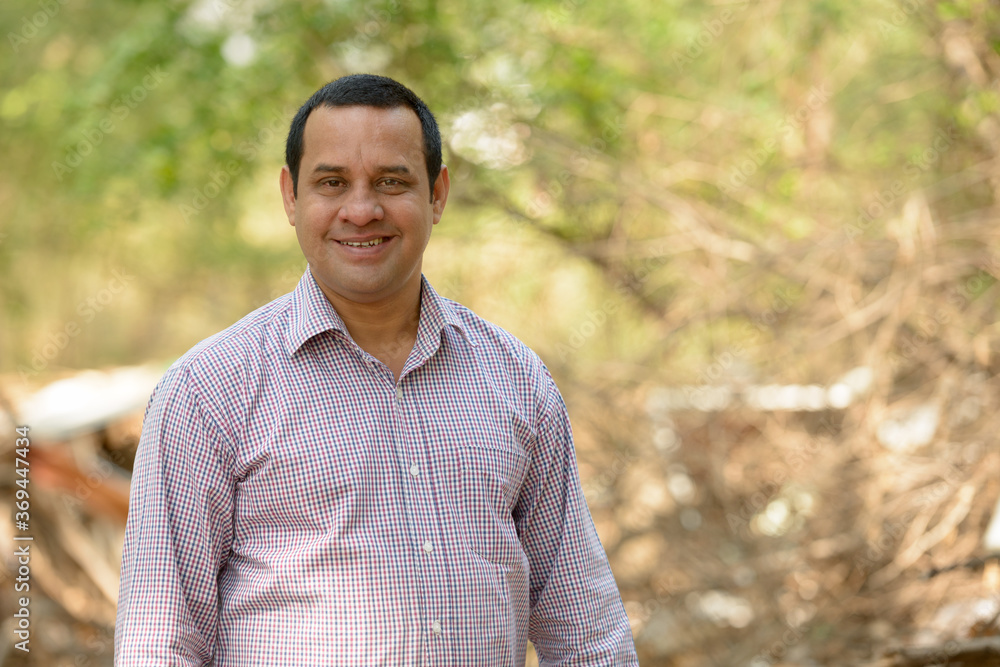 Portrait of happy overweight Indian businessman at the park outdoors Portrait of happy overweight Indian businessman at the park outdoors