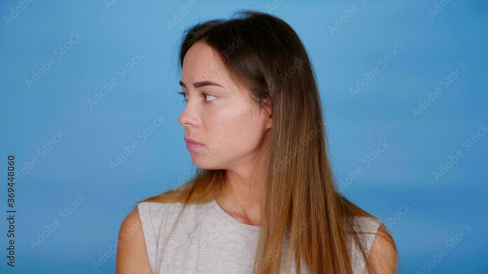 Beautiful woman in gray t-shirt looks around on blue background with copy space. 4K slow motion footage Beautiful woman in gray t-shirt looks around on blue background with copy space. 4K slow motion footage