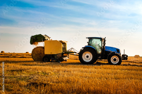 Tractor with bale machine for harvesting straw in the field and making large round bales. Agricultural work  harvesting hay on the hills in a summer field