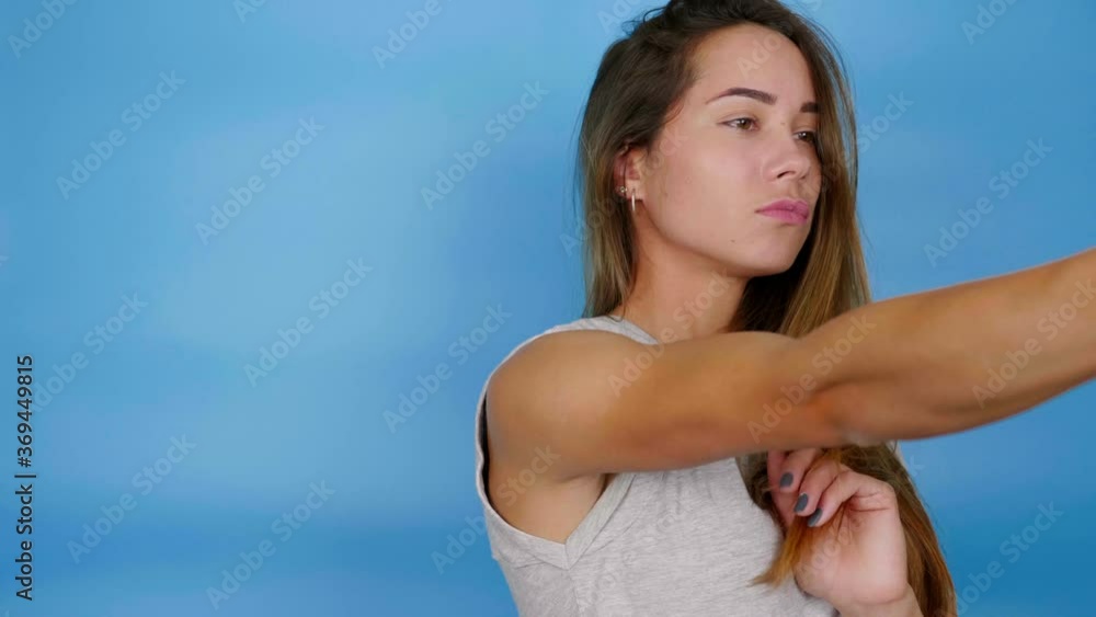 Beautiful woman in gray t-shirt poses and takes pictures of herself on selfie camera smartphone. Girl straightens hair on blue background with copy space. 4K slow motion footage Beautiful woman in gray t-shirt poses and takes pictures of herself on selfie camera smartphone. Girl straightens hair on blue background with copy space. 4K slow motion footage