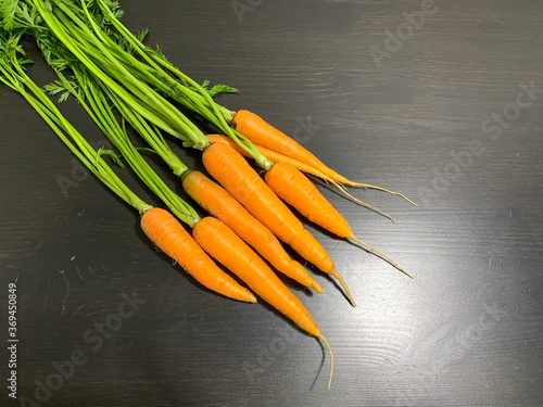 A bunch of fresh carrots on a black wooden table. Healthy food, vegetable harvest, proper nutrition, vitamins, vegetarianism.