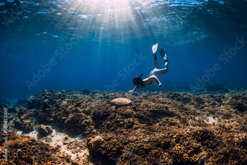 Woman with fins swimming underwater with big turtle.