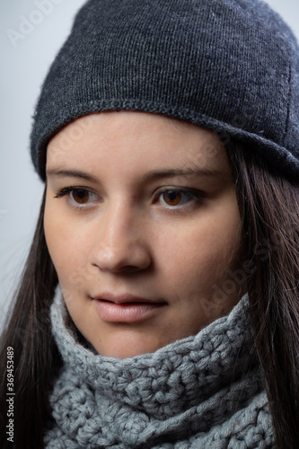 Closeup studio shot of a young lady. She is wearing winter clothes like scarf and hood. She is looking to one side.