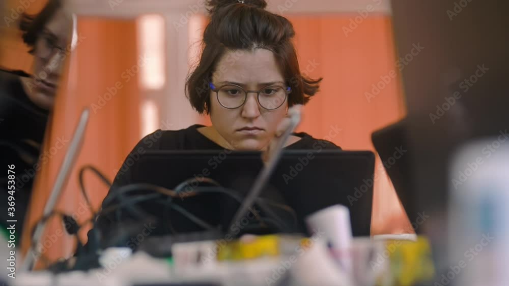 sad calm woman in glasses sitting at office working by the laptop irrl. making grimace. company worker at messy workplace. female manager working with computer data. tired sad calm woman in glasses sitting at office working by the laptop irrl. making grimace. company worker at messy workplace. female manager working with computer data. tired
