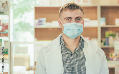 Pharmacist man in medical mask and white coat on the background of the pharmacy counter