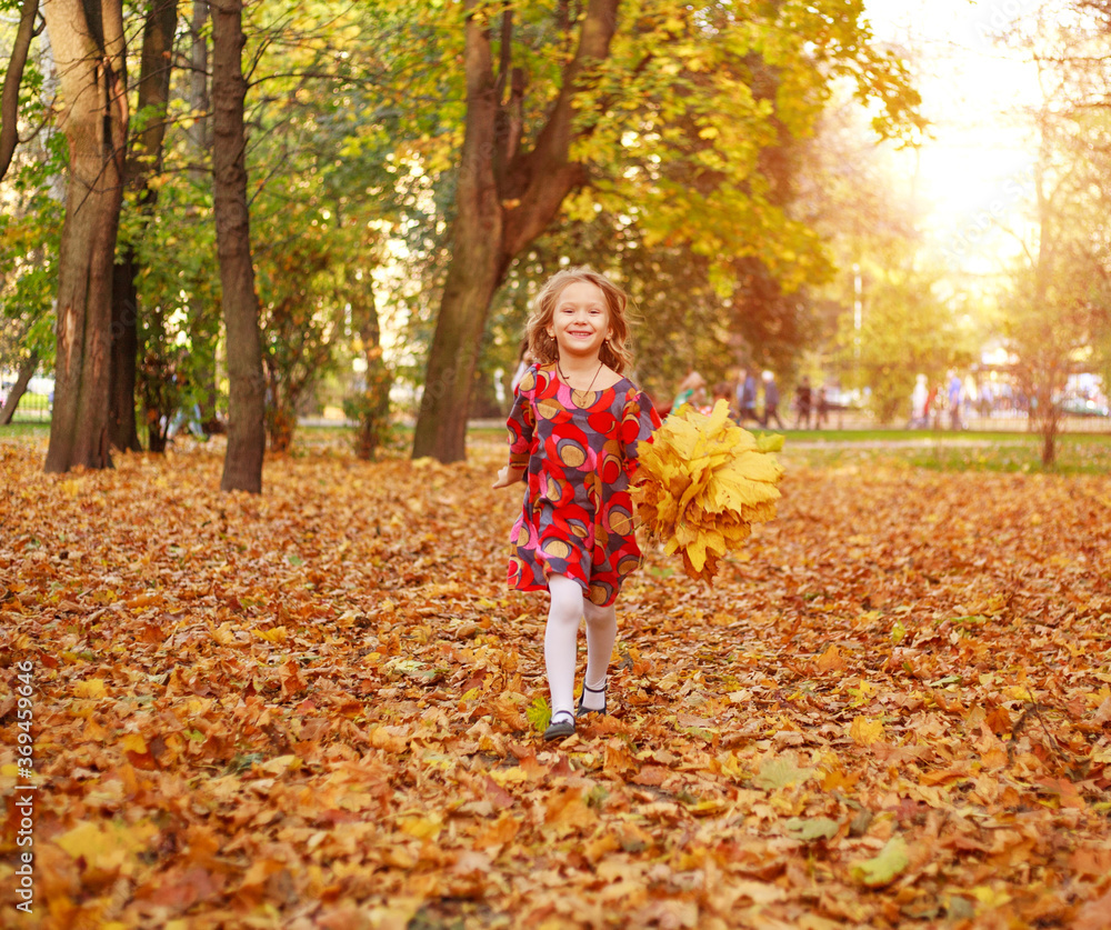 Portrait of happy joyful running child girl on fallen yellow autumn foliage in autumn city forest park in rays of sunset light Portrait of happy joyful running child girl on fallen yellow autumn foliage in autumn city forest park in rays of sunset light