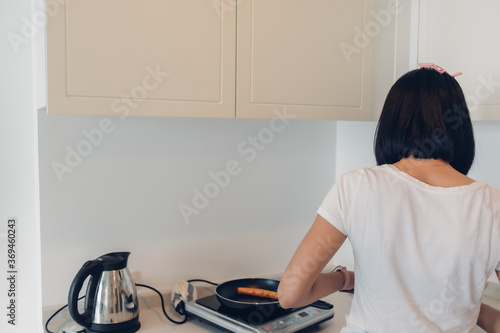 Asian woman is cooking simple breakfast in white cozy kitchen.