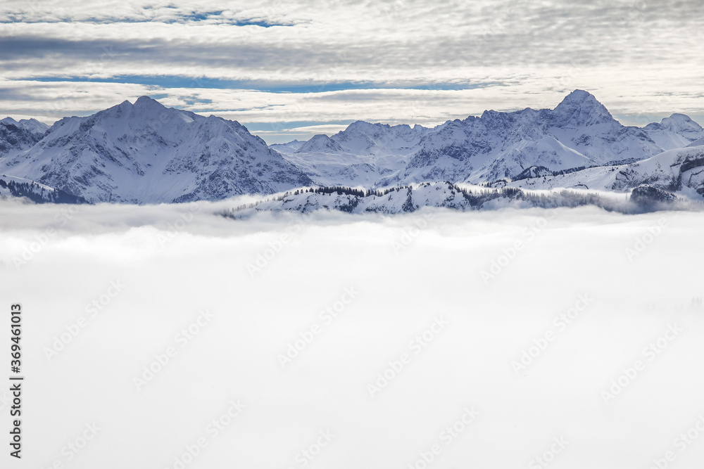 Snow covered mountains with inversion valley fog and trees shrouded in mist. Scenic snowy winter landscape in Alps, Allgau, Kleinwalsertal, Bavaria, Germany.