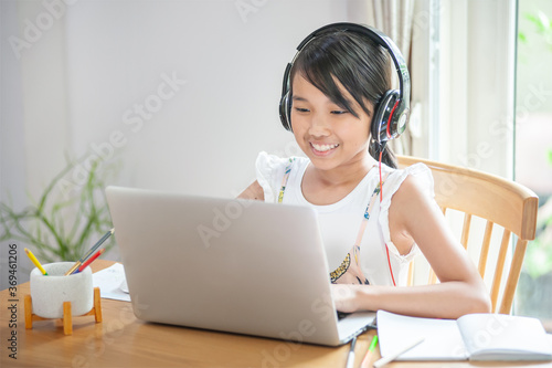 Smiling Little asian girl using laptop to learning onlne at home and typing on keyboard homeschool concept
