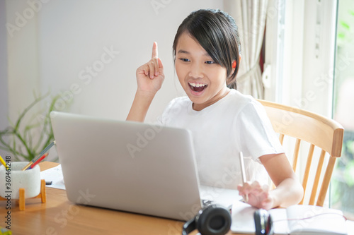 smiling asian girl using  laptop and happy to learn online at home and wearing white t-shirt photo