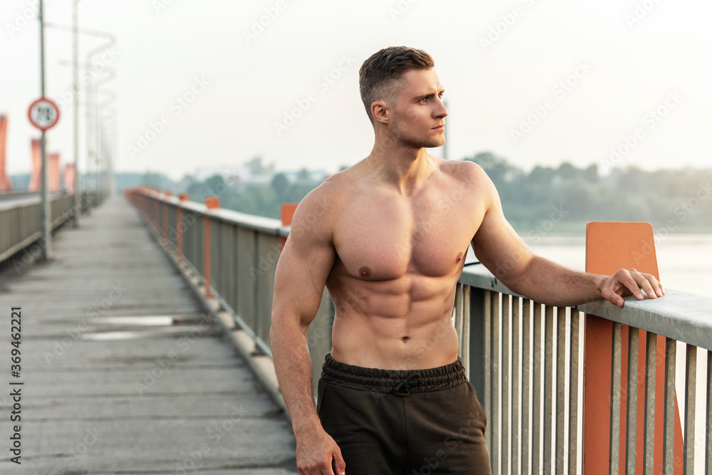 Obraz premium Muskularny mężczyzna z nagim torsem podczas treningu fitness na moście
