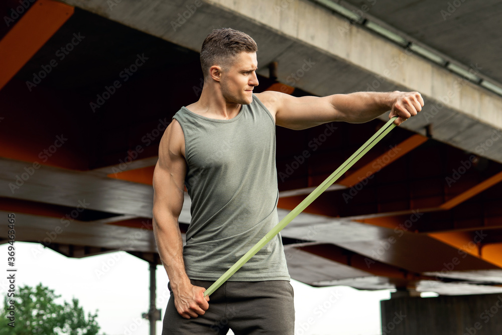 Muscular man during workout with a resistance rubber band on a street.
