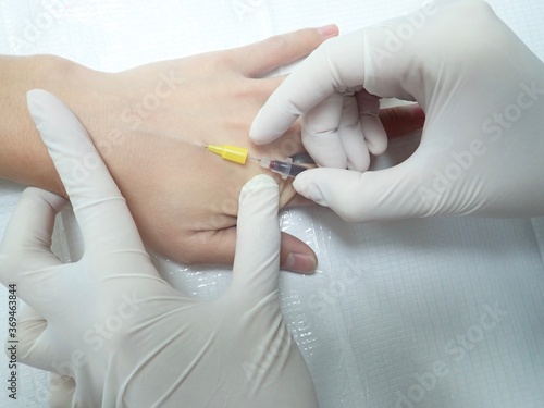 Close up Hand of nurse is inserting iv catheter or needle into a vein of patient for taking blood and give iv fluids.Takes a blood sample for tests. A needle in the vein  IV fluids  an injection into 