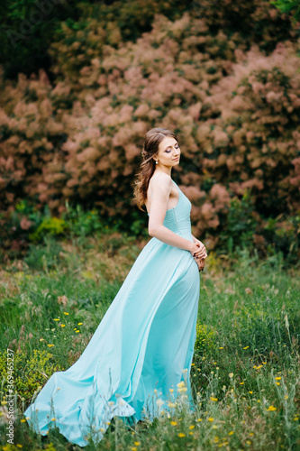 Happy girl in a turquoise long dress in a green park