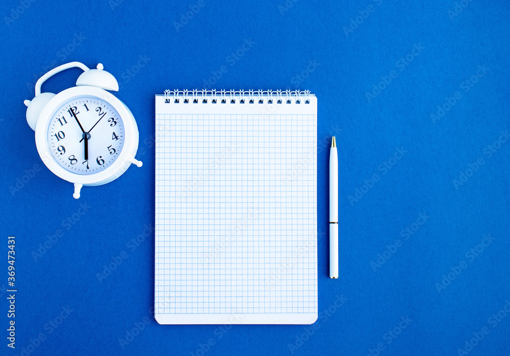 Notebook, white pen and white alarm clock on a blue background. Mockup for your design. Flatley. copy space Notebook, white pen and white alarm clock on a blue background. Mockup for your design. Flatley. copy space