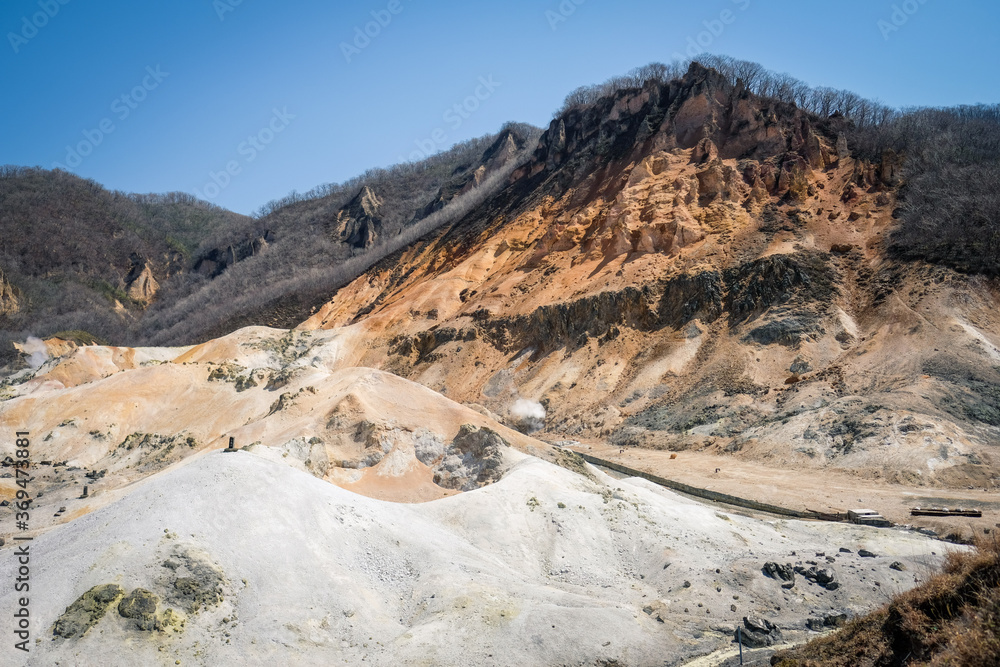 Beautiful view of Noboribetsu Jigokudani or Hell Valley in sunny day with blue sky in background. Autumn season and sulfur gas steaming out from ground.