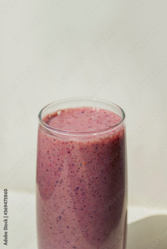 Blueberry pink smoothie in a transparent glass on light background with long shadows, top view. Milk Shakes. Healthy breakfast. Healthy food and vitamins concept Blueberry pink smoothie in a transparent glass on light background with long shadows, top view. Milk Shakes. Healthy breakfast. Healthy food and vitamins concept